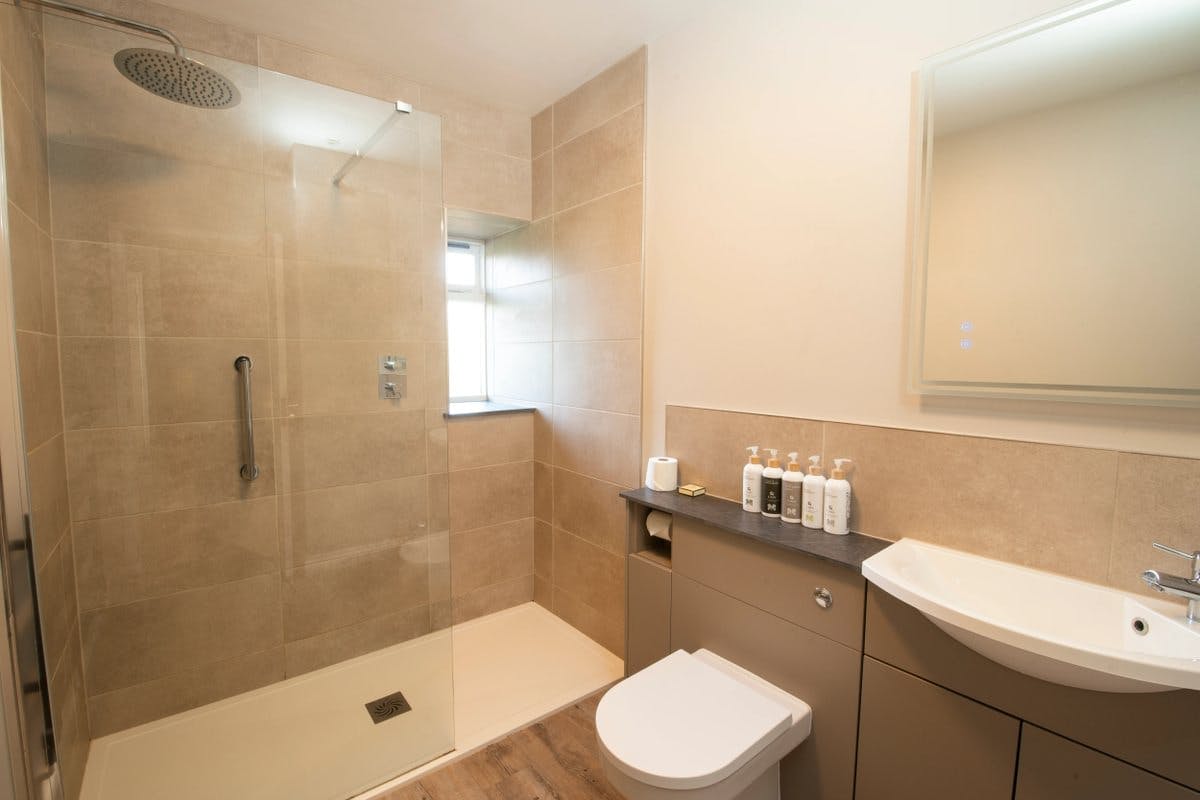Modern bathroom with a glass shower, beige tiles, toilet, sink, and toiletries on a counter.