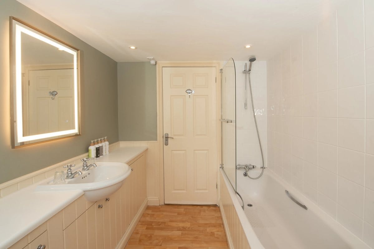 Modern bathroom with a lit mirror, sink, and bathtub with shower. Beige door and wood floor.