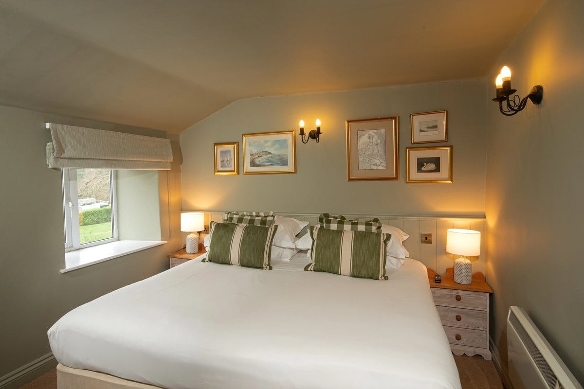 Cosy bedroom with a large bed, green-striped pillows, wall art, and warm lighting from lamps and sconces.