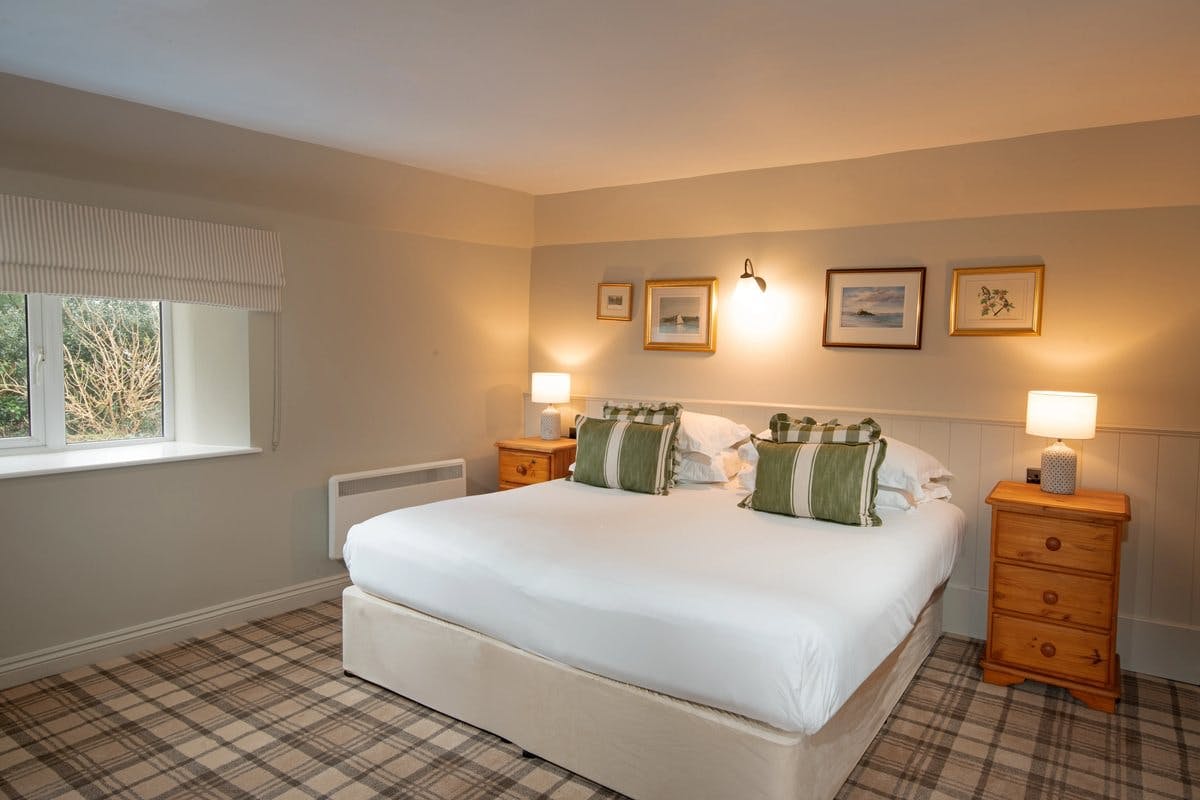 Cosy bedroom with a double bed, green-striped pillows, wooden nightstands, lamps, and framed art on beige walls.