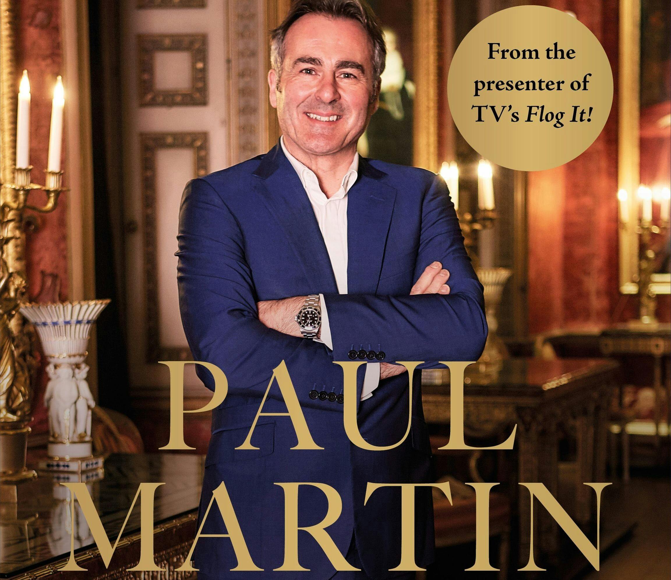 Man in a blue suit smiling with arms crossed, standing in an elegant room with candles. Text: "From the presenter of TV's Flog It!"