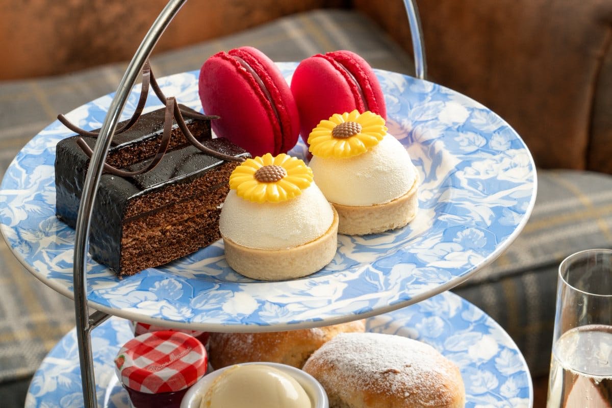 Tiered plate with chocolate cake, red macarons, and sunflower-topped pastries on blue floral china.