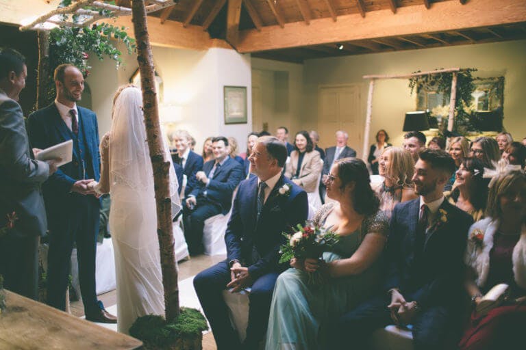 A couple saying their vows in front of all their friends and family during a wedding ceremony in the lounge at Careys Manor.