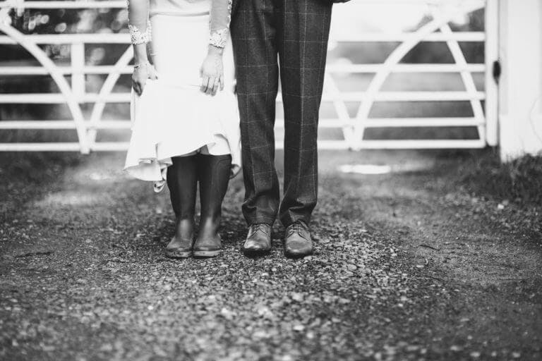 Close up of bride and groom's legs with bride wearing wellington boots under wedding dress