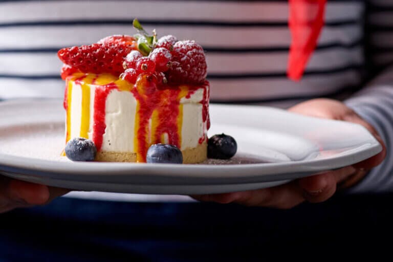 Waiter holds plate with fruit cheesecake dripping in fruity sauce