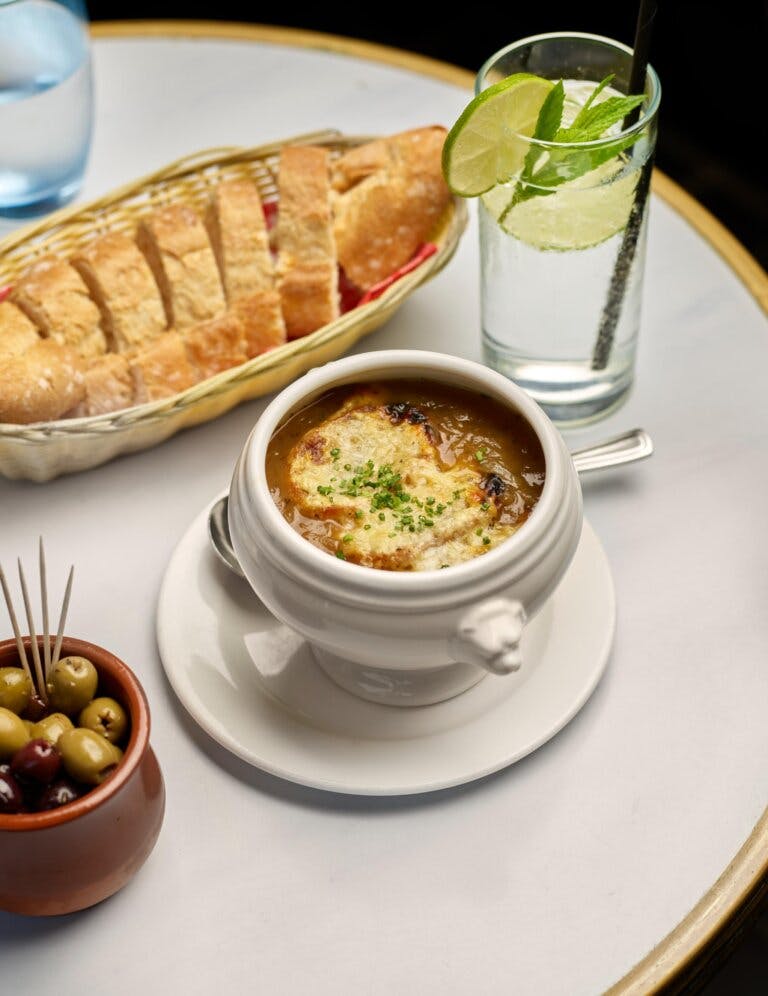 French onion soup, garlic bread, olives and drink on round table in restaurant