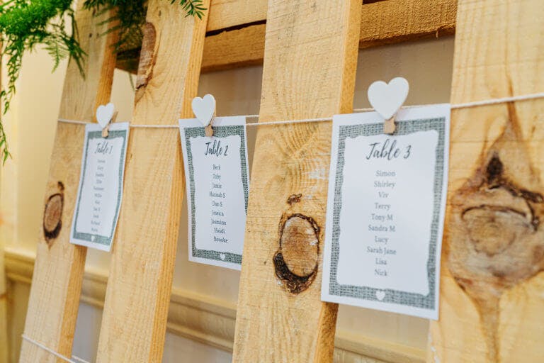 A wood palette with three table plan sheets attached to it with wooden clothes pegs.