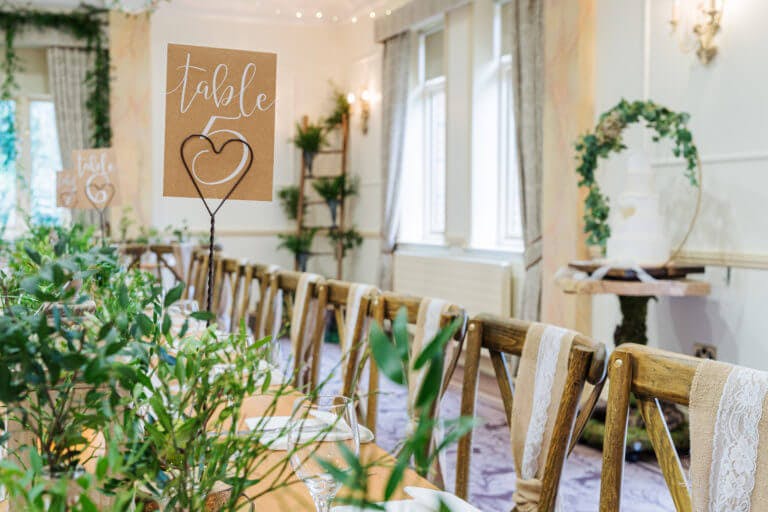 a long table with set up for a wedding breakfast with lots of green foliage. the table is set with chiavari chairs with lace sashes.