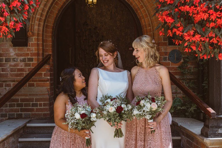 Bride stands with two bridesmaids and laughs on staircase at entrance to hotel wedding venue Careys Manor Hotel & SenSpa
