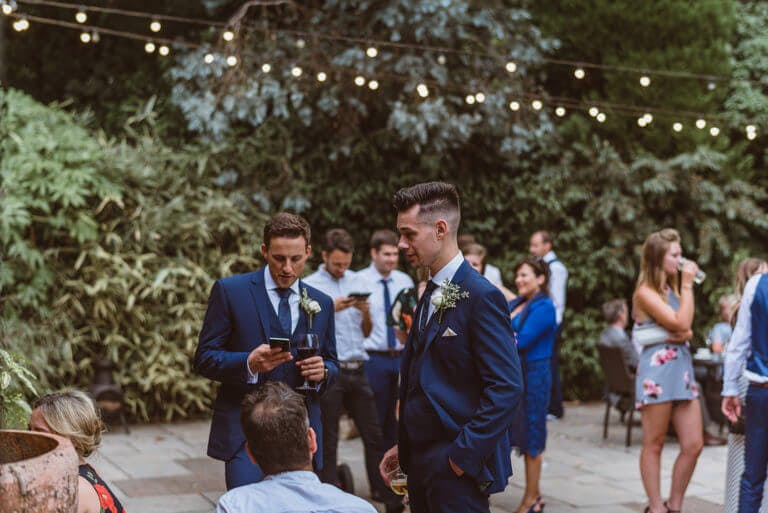 Wedding guests gather outside in grounds of hotel wedding venue beneath string of lights