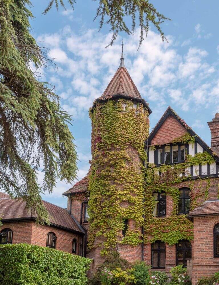 Exterior of Victorian manor house hotel with tall tower covered in green ivy on sunny day
