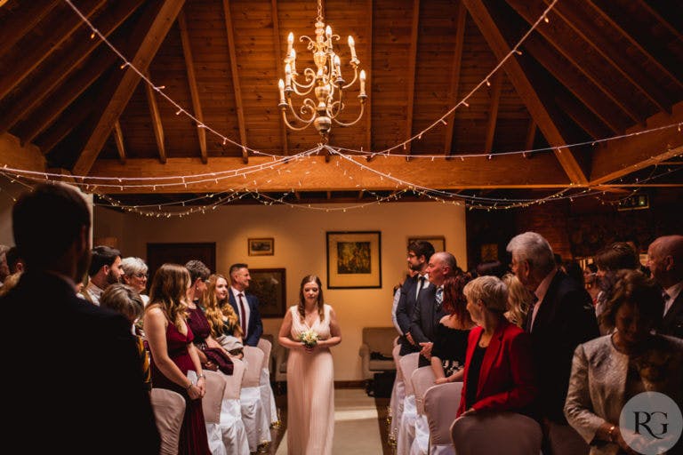Bride walking up the aisle alone carrying bouquet on wedding day as wedding guests look on happily