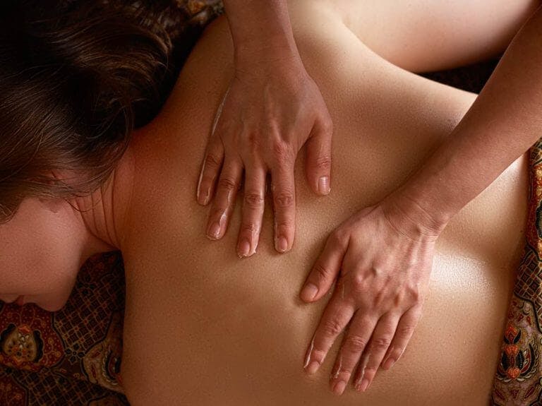 Woman lies face down receiving back massage at spa