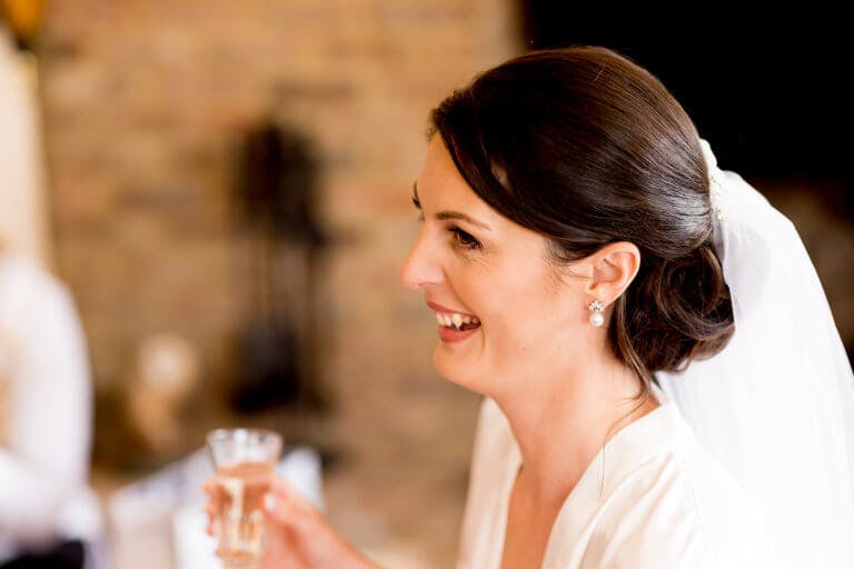 The Bride, Hayley, smiles whilst enjoying a glass of champagne whilst getting ready before her wedding at Hampshire wedding venue Careys Manor