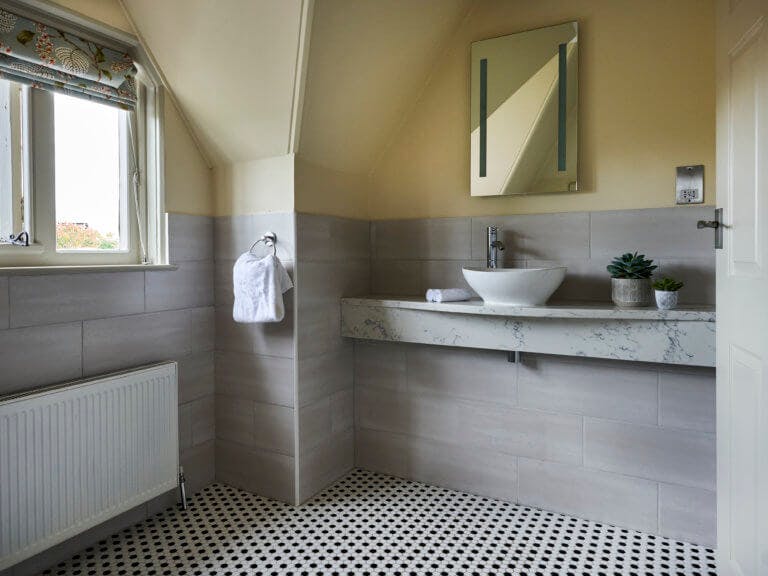Modern bathroom in hotel with yellow walls and black and white checked floor tiles. Marble effect sink area.