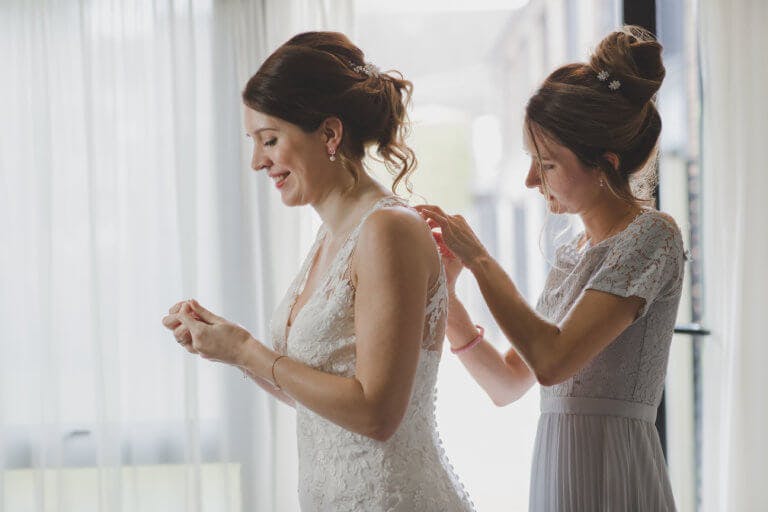 Bridesmaid doing up the necklace of the bride before the ceremony at Hampshire wedding venue Careys Manor.