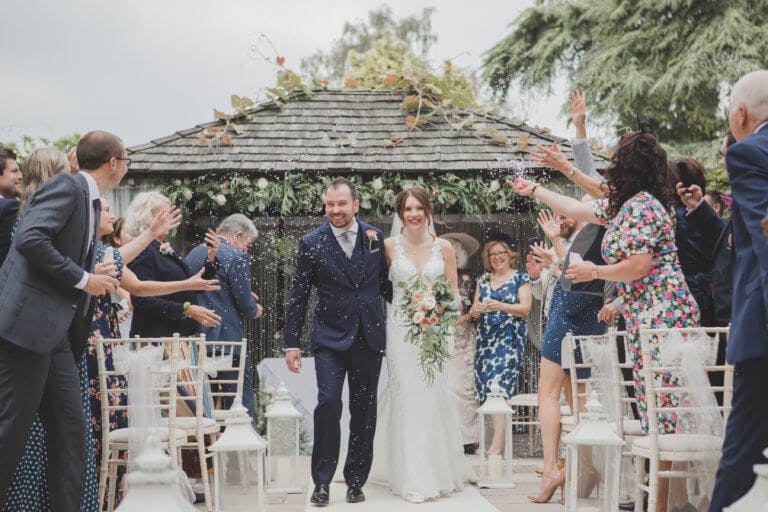 The Bride and Groom walk up the aisle following the ceremony with confetti in the air. at Hampshire wedding venue Careys Manor Hotel
