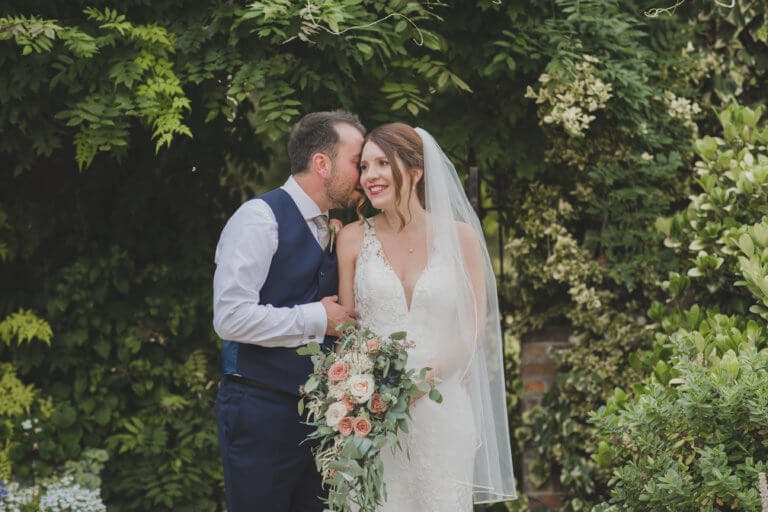 The Groom whispers into the Brides ear in the gardens of Hampshire wedding venue Careys Manor Hotel