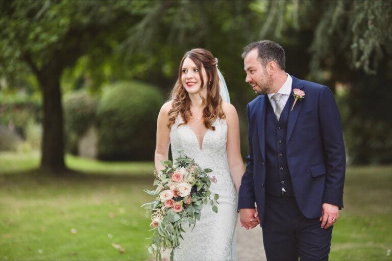 The Groom leans in to speak to the Bride as they walk together in the Gardens of Hampshire Wedding The Bride and Groom walk hand-in-hand up the drive at the front of Hampshire wedding venue Careys Manor Hotel