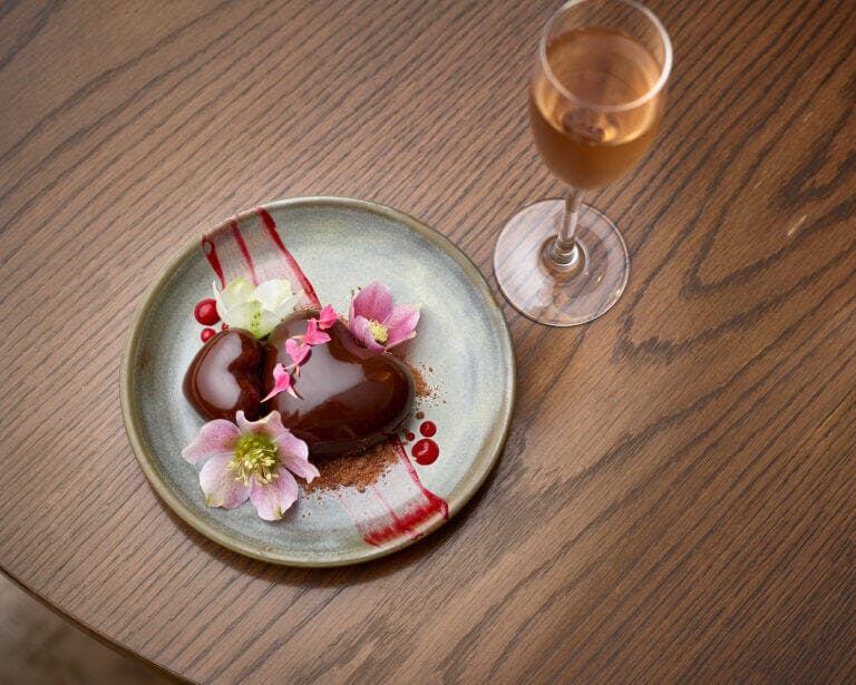 Heart shaped chocolate glazed dessert and glass of pink champagne on wooden table in Cambium restaurant, Brockenhurst for Valentine's Day