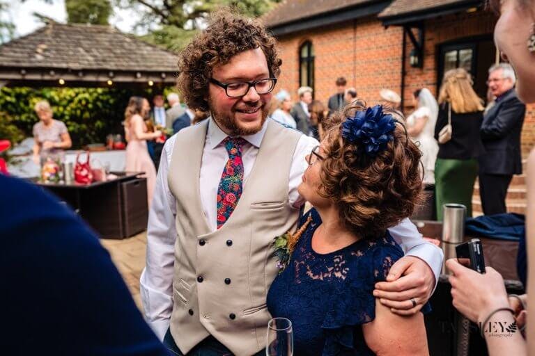 Groom smiles and puts his around a wedding guest
