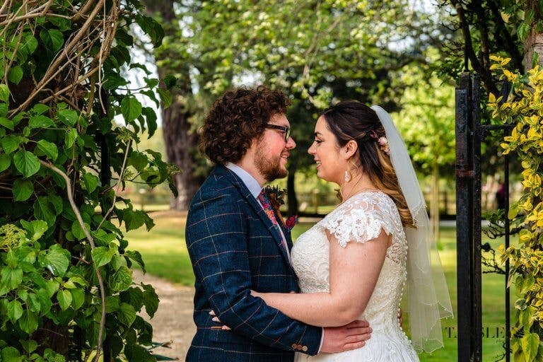 Bride and Groom stand facing each other under an archway of greenery in the garden
