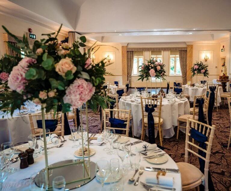 Wedding breakfast room set up with tall vases of pink flowers