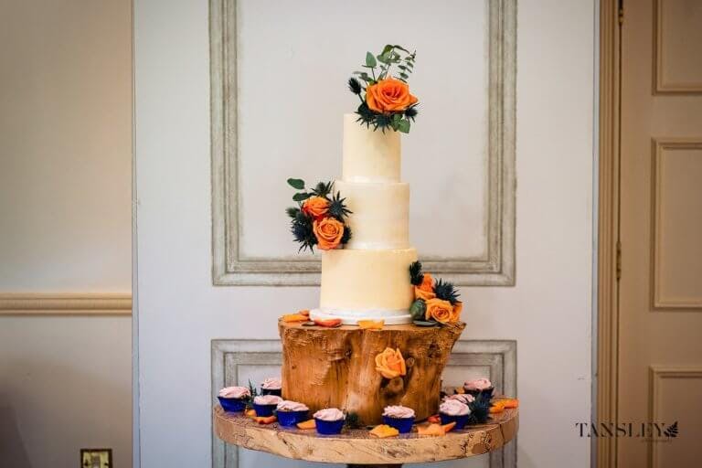Three tier wedding cake surrounded by cupcakes