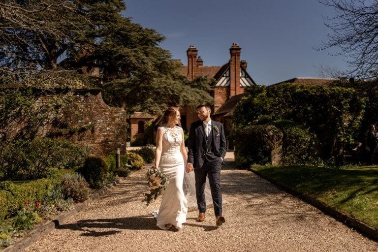 The bride and groom smiling as they walk away from the hotel with it in the background