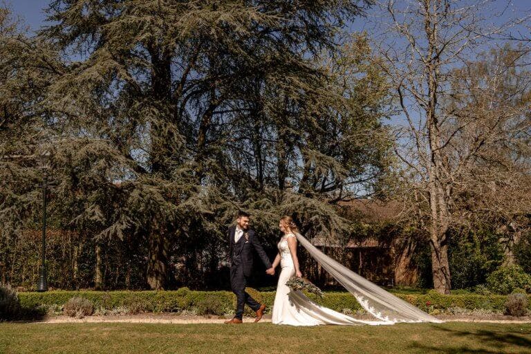 The bride and groom stroll hand-in-hand through the garden