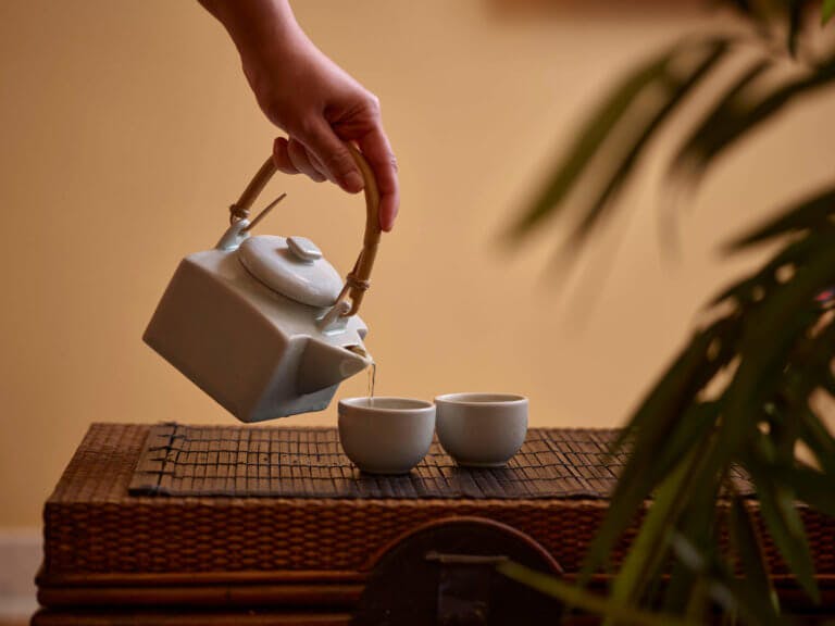 A SenSpa therapist pouring herbal tea from a traditional Thai tea pot with matching cups.