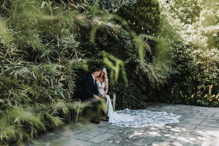 Bride and groom seen in through foliage posing for photos