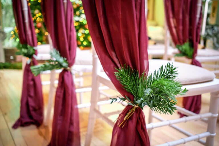 Wedding ceremony wooden chairs with burgundy sashes and evergreen sprig details