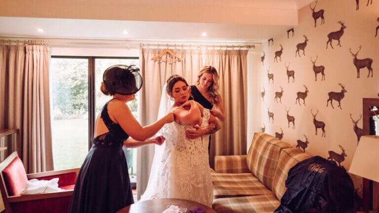 The bridesmaids help the bride into her dress