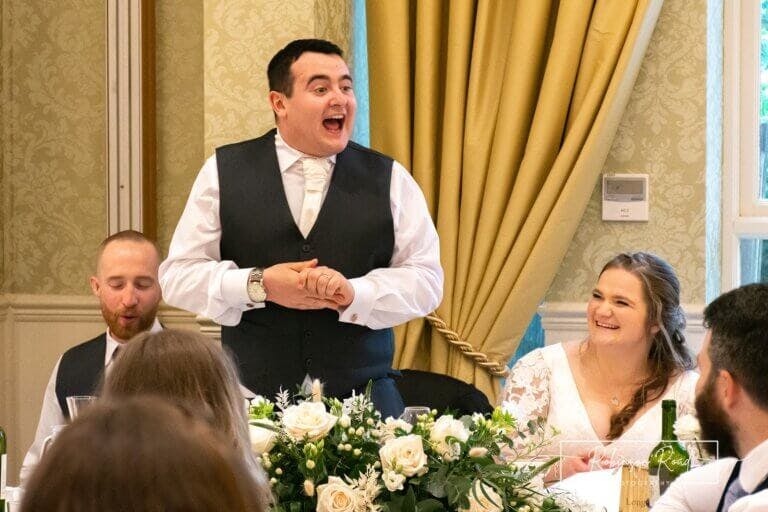 Groom standing giving speech at wedding next to seated bride at Careys Manor Hotel & SenSpa wedding venue in The New Forest