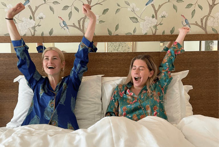 Girls' retreat at a hotel. they are both in white sheets and wearing silk-patterned pyjamas.