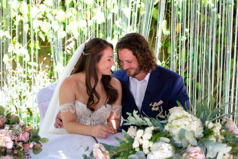 Chelsie and Chris sign the register sat down surrounded by white flowers