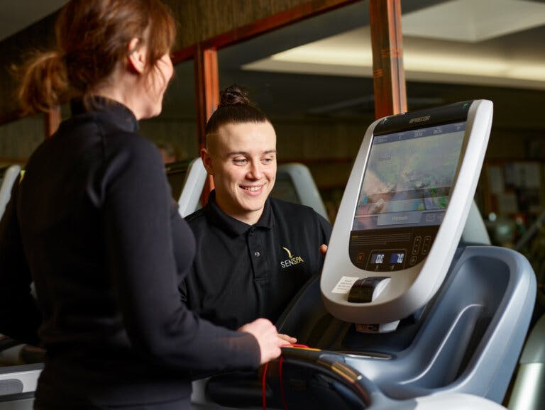 Personal Trainer stands next to a gym member on the treadmill