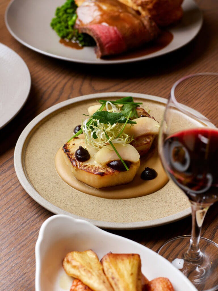 Celeriac dish for Sunday lunch at Cambium restaurant in Brockenhurst, with glass of red wine, parsnips and beef dish surrounding