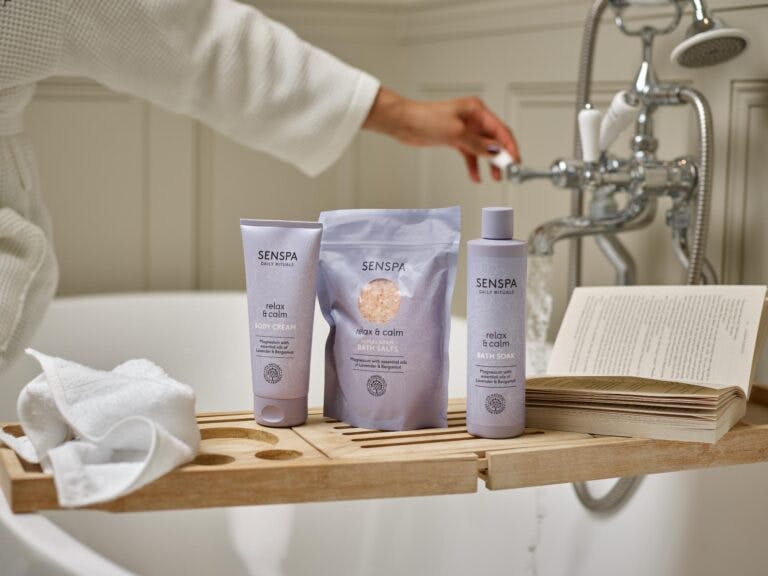 Woman in robe runs bath with a selection of SenSpa products