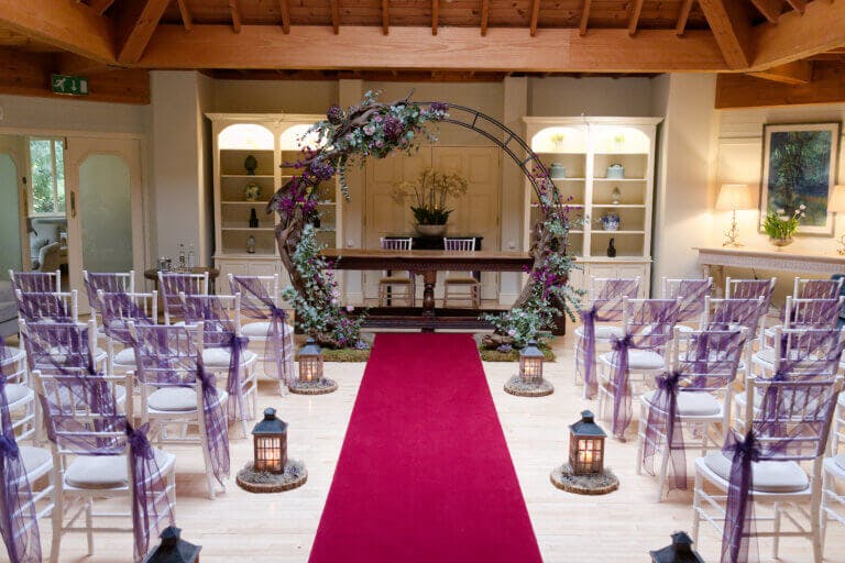 The lounge set for the wedding ceremony with a red carpet and a moon gate with floral details.