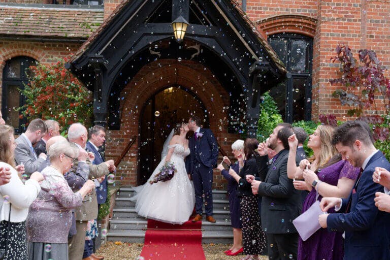 The bride and groom share a kiss at the main entrance after the ceremony to be welcomed by their guests who are throwing confetti