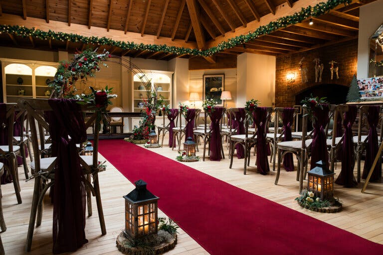The lounge set for Maxine & Alastair's wedding ceremony at Hampshire wedding venue Careys Manor Hotel & SenSpa, photographed from the side of the room. A red carpet is placed down the aisle with lanterns and a moon gate is behind the registrars table.