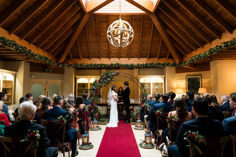 Looking down the aisle to the bride and groom facing each other, holding hands under the moon arch at Hampshire wedding venue Careys Manor Hotel & SenSpa.