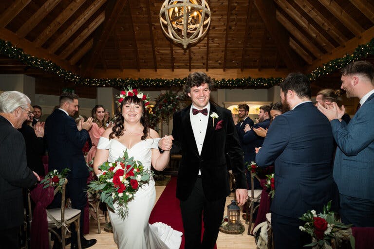 The bride and groom smile as they walk hand in hand out of the wedding ceremony at Hampshire wedding venue Careys Manor Hotel & SenSpa.