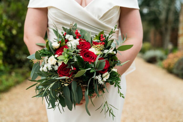 Close up of the bride, Maxine, holding her bouquet of red, white and green florals at Hampshire wedding venue Careys Manor Hotel & SenSpa.