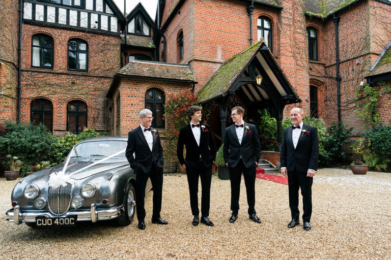 The grooms party stand by the vintage car at the front of Hampshire wedding venue Careys Manor Hotel & SenSpa.