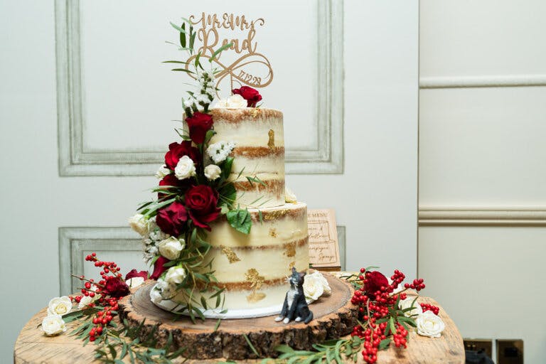 3 tier wedding cake dressed with red flowers, 'Mr & Mrs Read' topper and figurine of their cat.