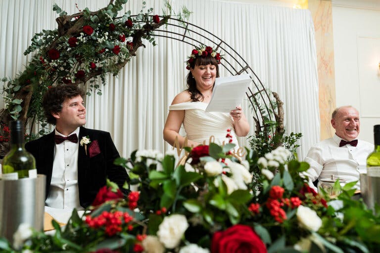 The bride stands at the top table and smiles reading her speech