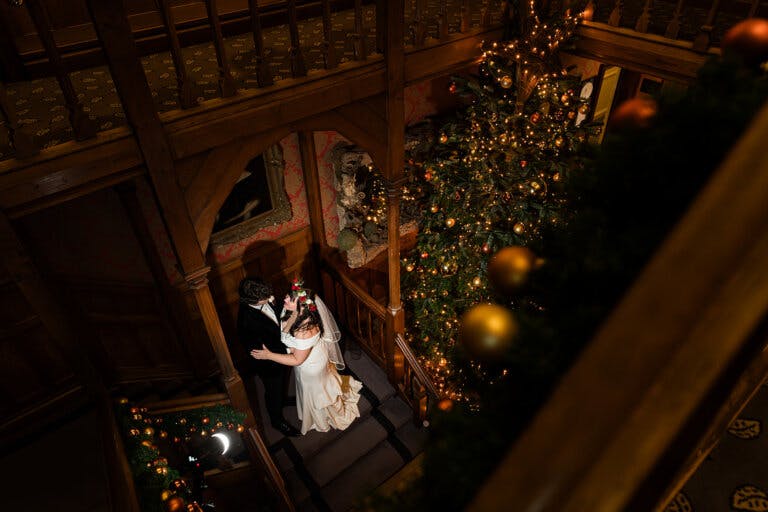 The bride and groom are stood on the staircase by the Christmas tree, photographed from above.